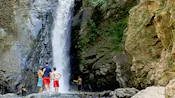 People stand in front of a tall waterfall pouring down a rock face 